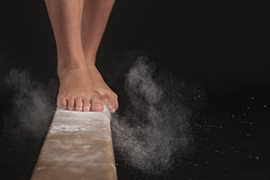 A gymnast lands a jump on a balance beam.